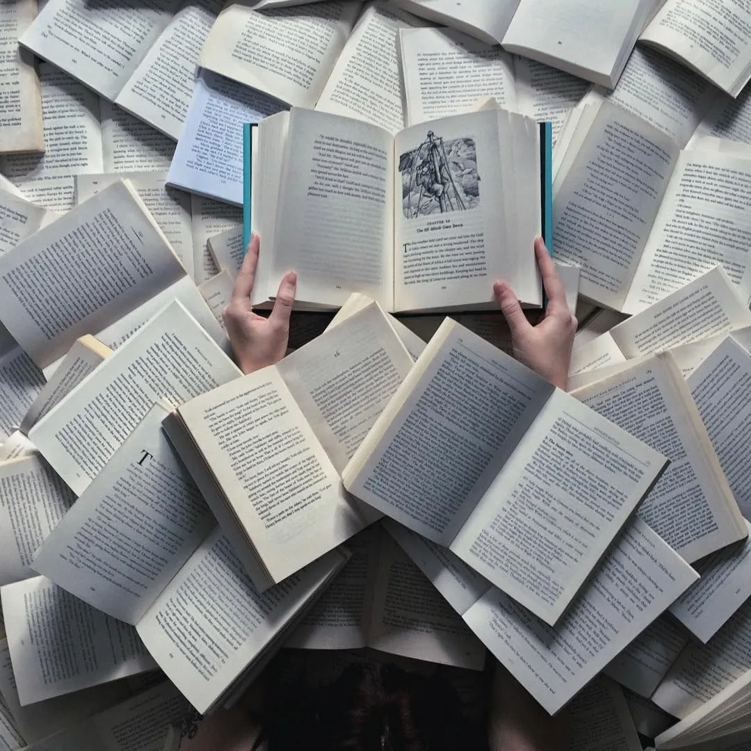 Hands holding an open book above a spread of open books
